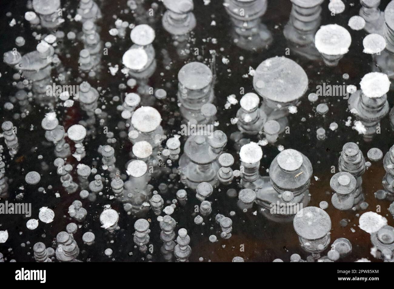 Im EIS eines Teichs eingefrorene Luftblasen bilden ein abraktes Muster Foto Stock