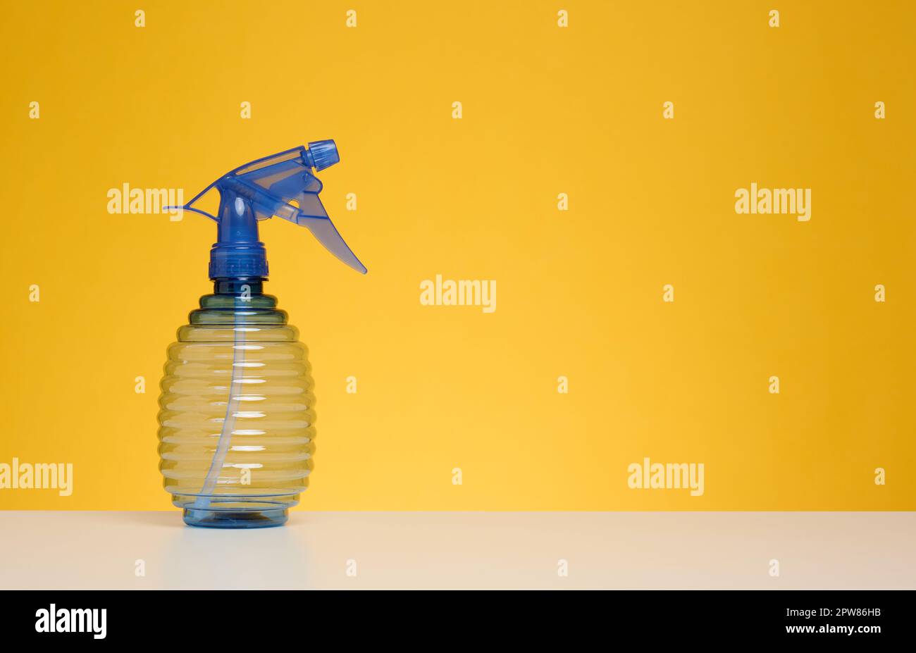 Bottiglia di plastica con spray per stirare i vestiti, innaffiatura delle piante su un tavolo bianco, fondo giallo. Spazio di copia Foto Stock