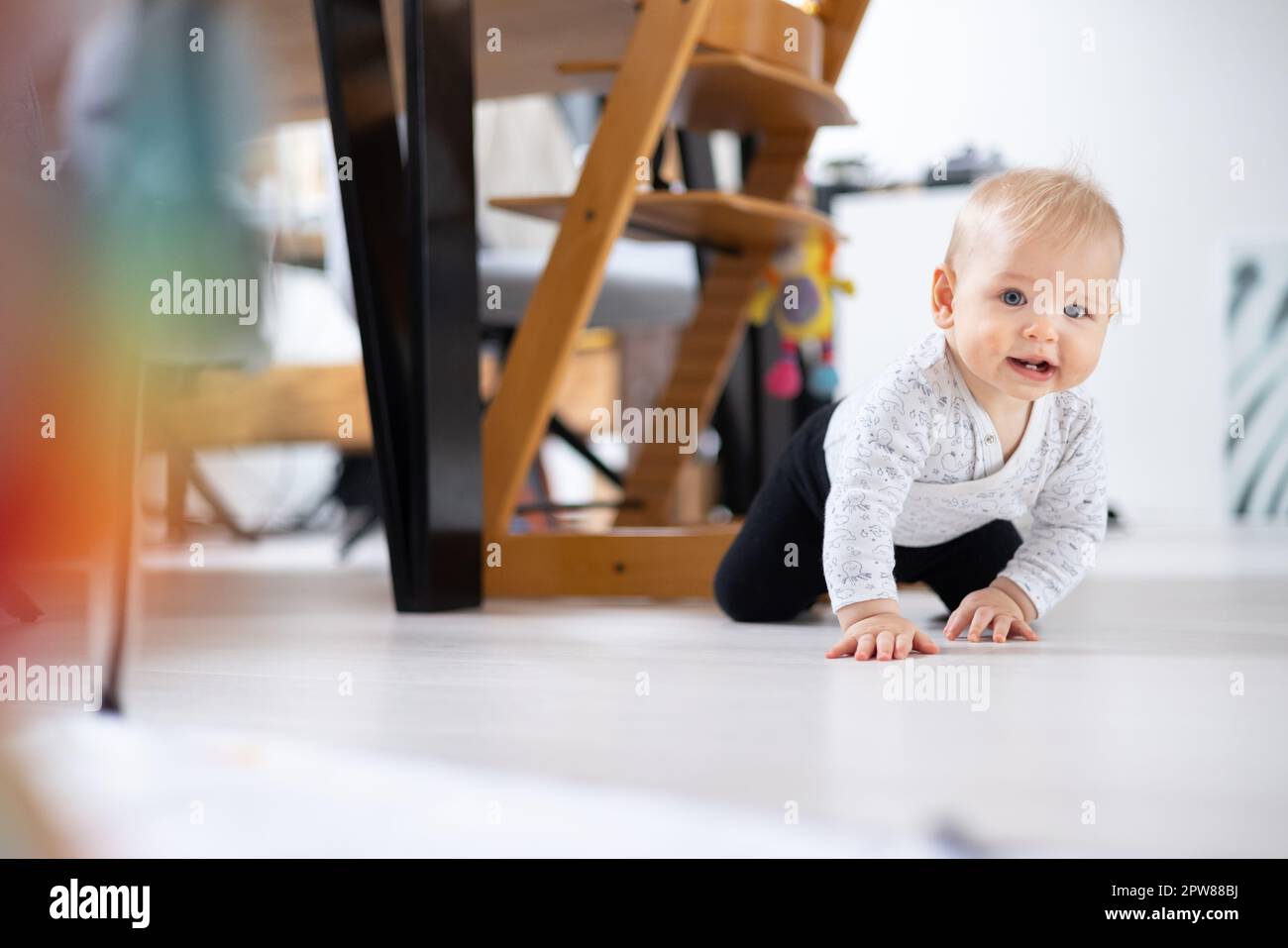 Carino bambino ragazzo che striscia sotto il tavolo da pranzo a casa. Il bambino gioca a casa. Foto Stock