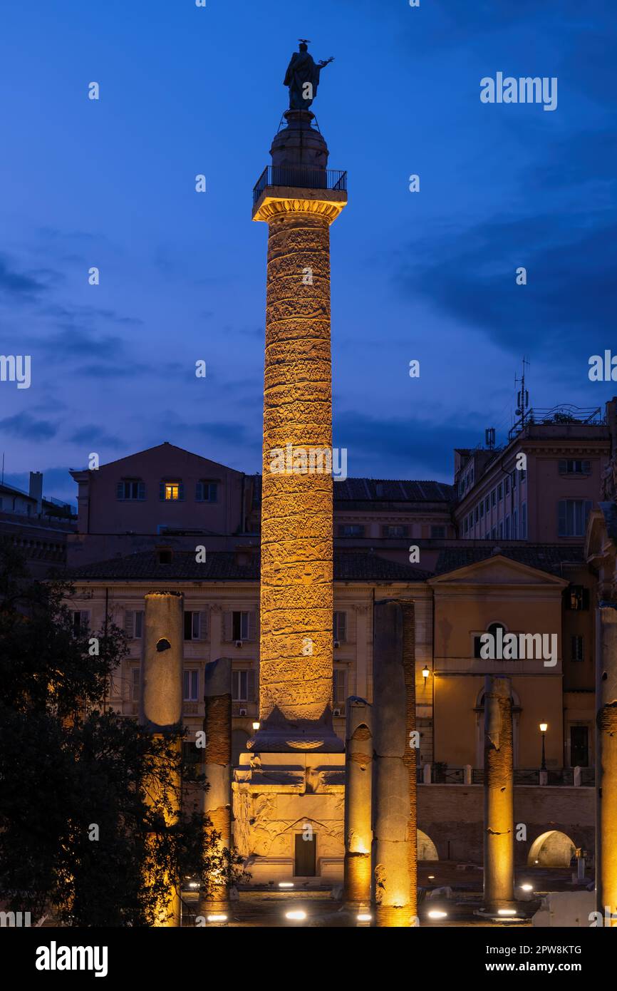 La colonna Traiana del 113 d.C. al Foro Traiano (Foro di Traiano) illuminata di notte nella città di Roma. Antico punto di riferimento adornato con bassi a spirale Foto Stock