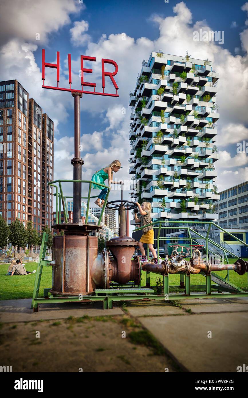 Paesi Bassi, Eindhoven, Strijp-S. I bambini giocano con i vecchi macchinari davanti alla Torre Trudo dell'architetto italiano Stefano Boeri. Foto Stock