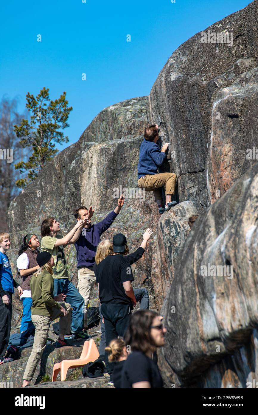 Giovane uomo bouldering o arrampicata su roccia con gli spoter che si fissano a Humallahti scogliere o Humallahden kalliot nel quartiere Meilahti di Helsinki, Finlandia Foto Stock