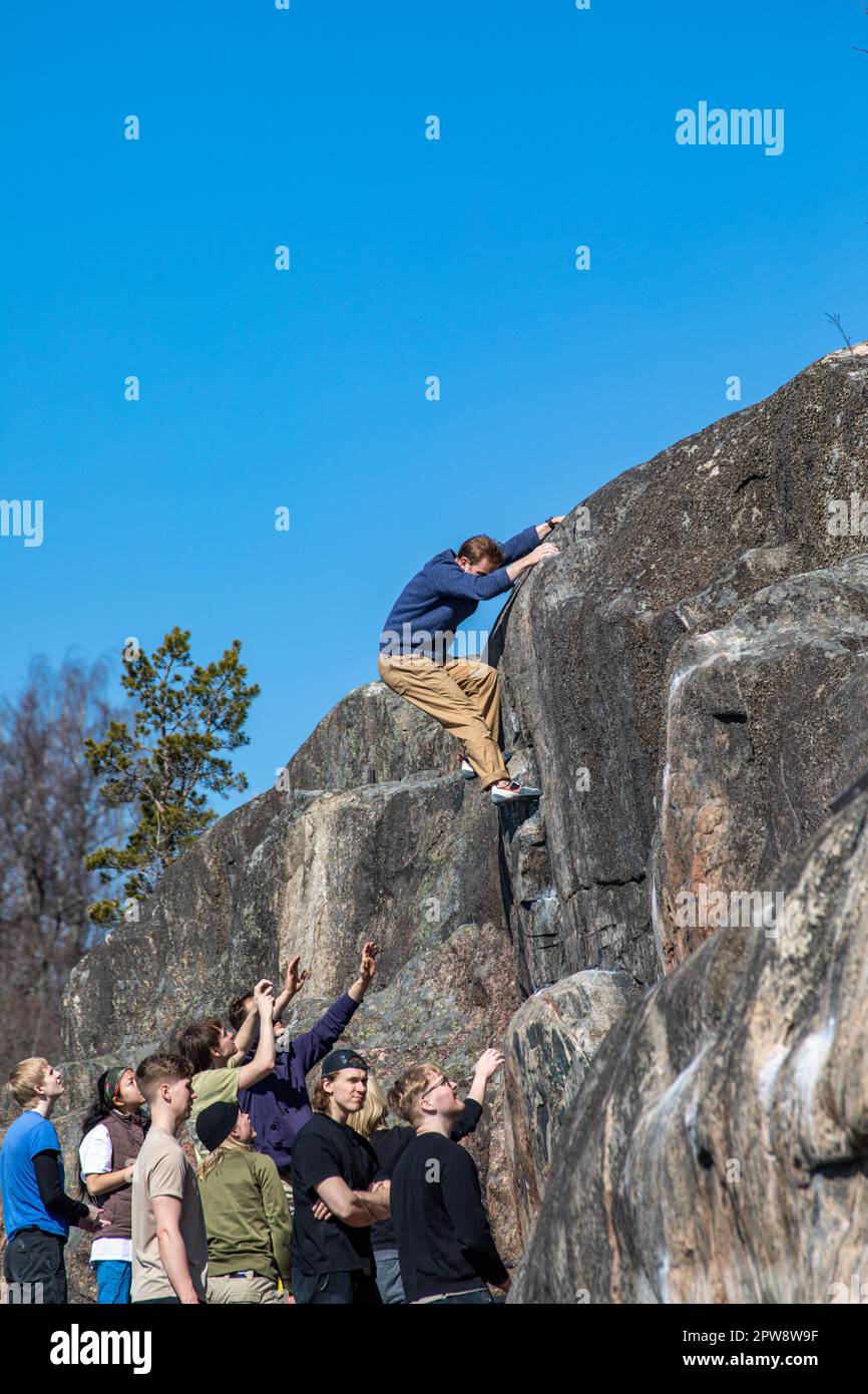 Giovane uomo bouldering o arrampicata su roccia con spoter di sicurezza sotto a Humallahden kalliot o Humallahti scogliere a Meilahti, Helsinki, Finlandia Foto Stock