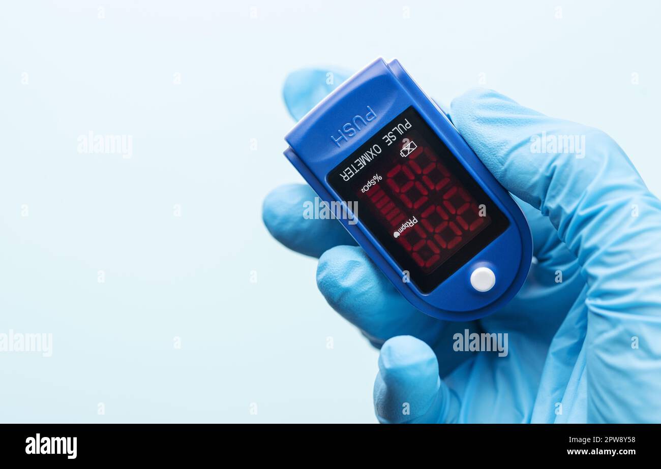 Pulsossimetro in mano del medico con guanto su sfondo blu. Una mano in un guanto medico contiene un dispositivo per la diagnostica sanitaria Foto Stock