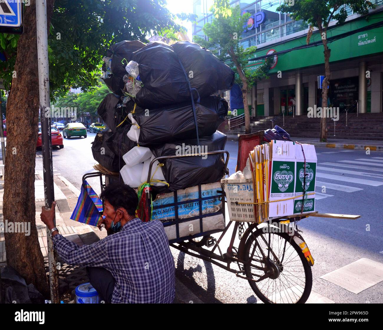 Lavoratori, Bangkok, Thailandia, Asia. Un vecchio collezionista maschile di materiali riciclati, come bottiglie di plastica e cartone, si riposa nel distretto di Silom. Il suo triciclo è carico di sacchi di materiali raccolti. I truffatori come questo riducono i rifiuti per le strade della città anche se i loro guadagni sono bassi. Alcuni lavenger che sono anche chiamati SA leng, ricerca attraverso bidoni di rifiuti alla ricerca di bottiglie, lattine e cartone per il commercio di alimenti e altri beni in una cooperativa di riciclaggio. Alcuni vendono ciò che trovano. Lavoro, lavoratore, lavoro, lavoro, occupazione, guadagnare soldi, spazzatura scavenger, tema di povertà. Foto Stock