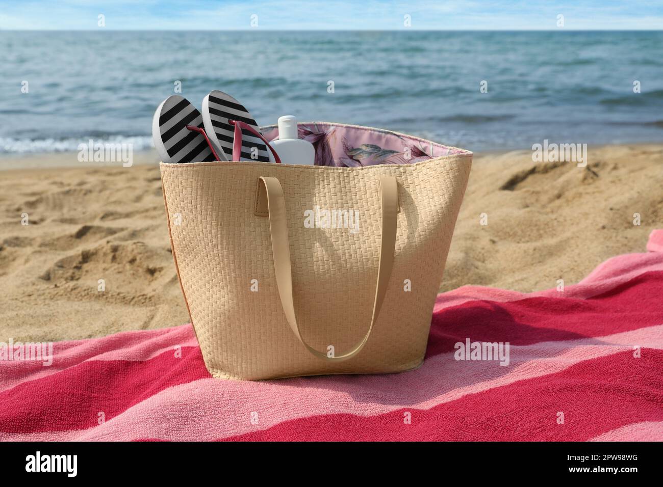 Asciugamano a strisce rosa con borsa, infradito e crema solare sulla spiaggia Foto Stock