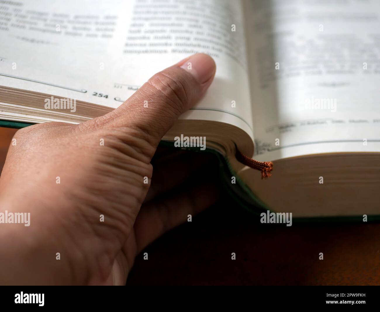 Un pollice che capovolgerà le pagine di un libro in fuoco poco profondo, priorità bassa educativa Foto Stock