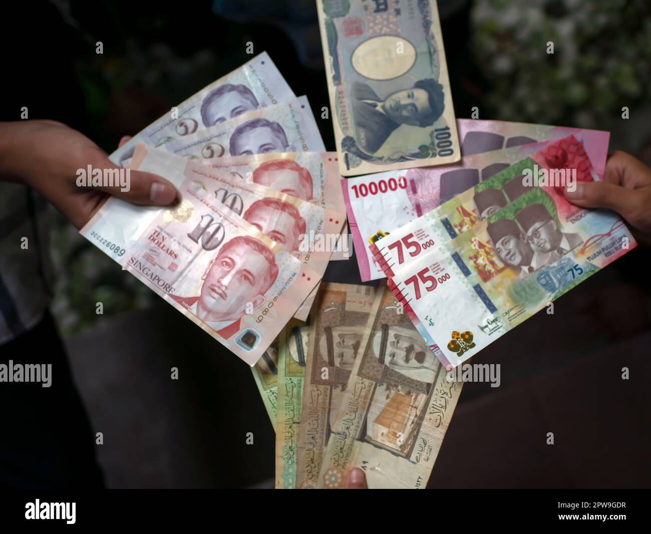 Bambino asiatico in possesso di rupia indonesiana, dollaro di Singapore, arabia Saudita riyal, e Giappone Yen denaro, poco focus Foto Stock