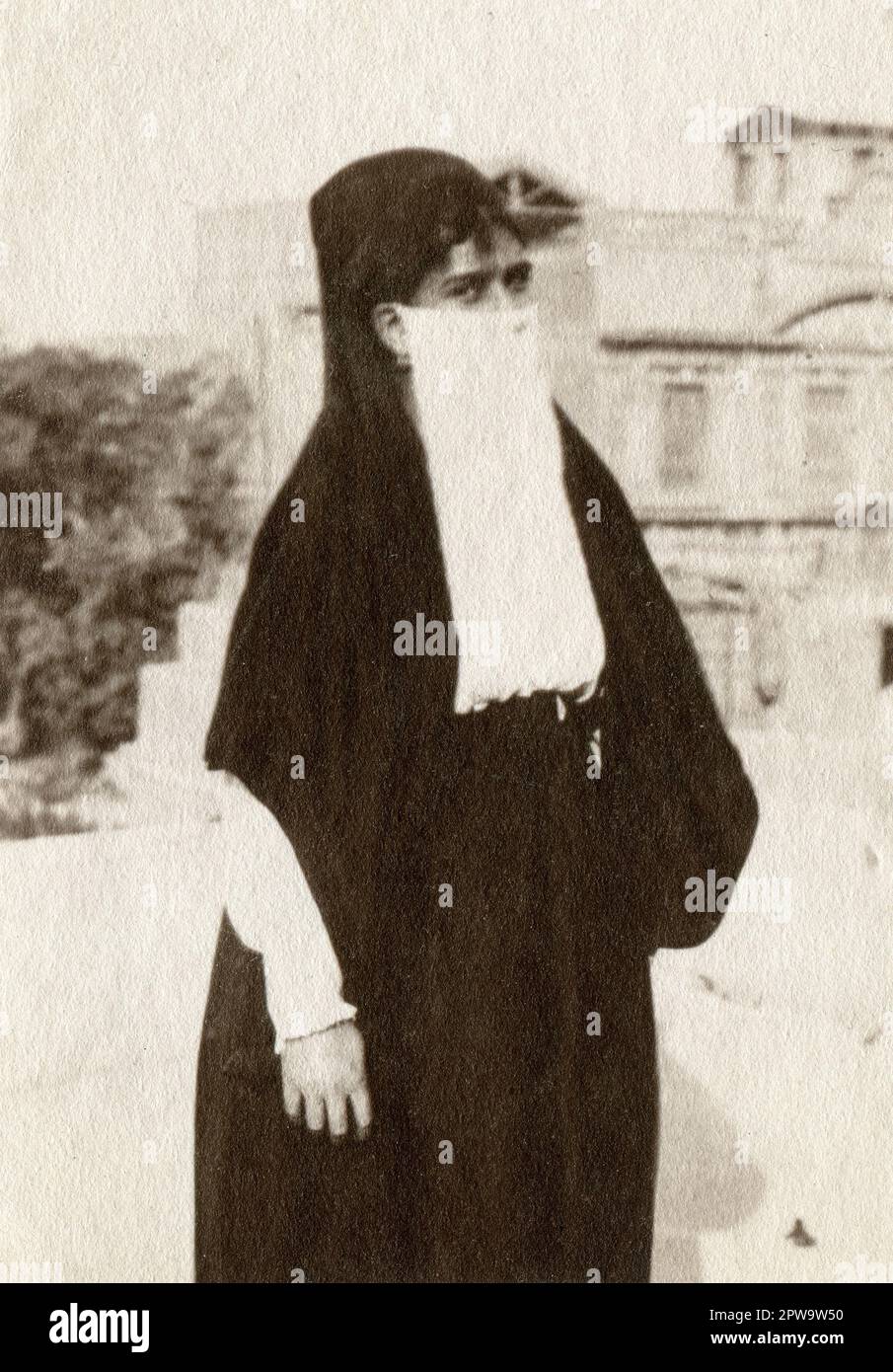 Egitto. Circa 1918. Una giovane donna che si posa per una fotografia, indossando al-habara, composta da una gonna a tutta lunghezza, una copertura per la testa, e una al-burqu’ bianca, una copertura per il viso. Foto Stock