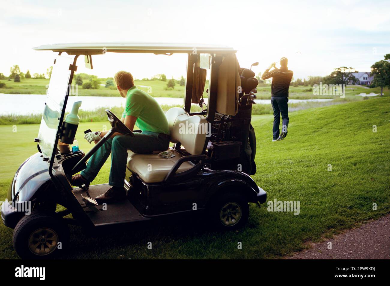 Golf andato. un uomo che guarda il suo amico giocare a golf mentre si siede in un golf cart. Foto Stock