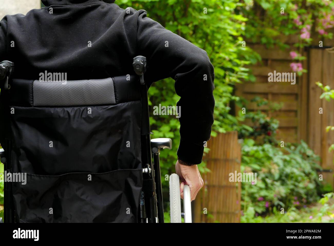 Una persona disabile su sedia a rotelle. Un uomo a mobilità ridotta in un vicolo con vegetazione. Foto Stock