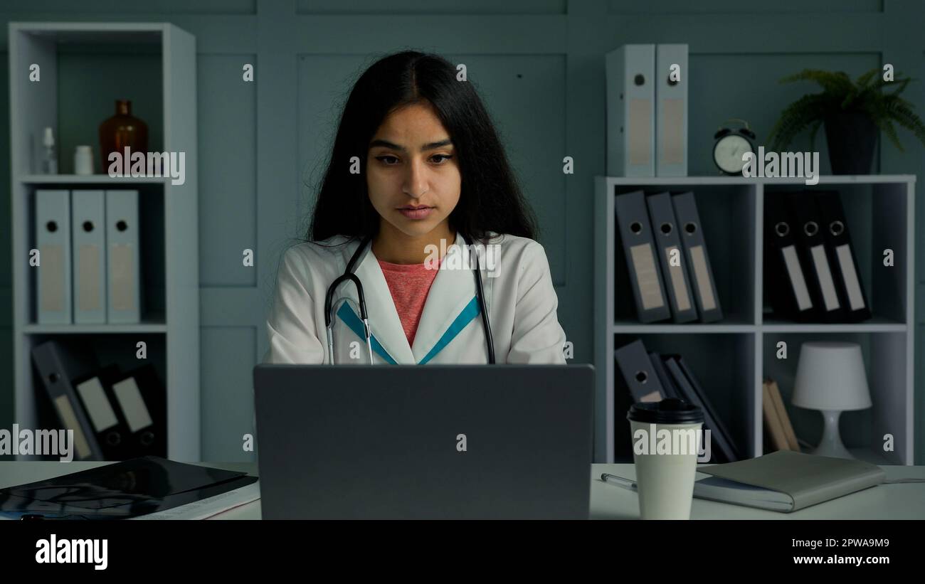Annoiato giovane donna medico intern medico femminile lavoro sul laptop controllare i risultati dei test dei pazienti online in medicina virtuale app digitando elettronica Foto Stock
