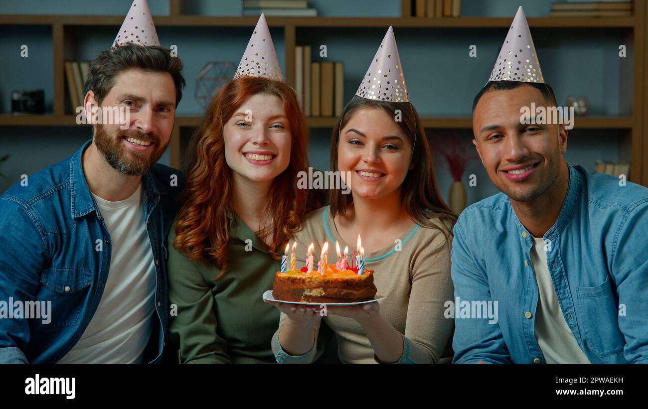 Amici in calotte festa celebrare evento festivo a casa diverse persone multirazziali uomini donne tenere torta di compleanno con candele. Ritratto di gruppo sorridente Foto Stock
