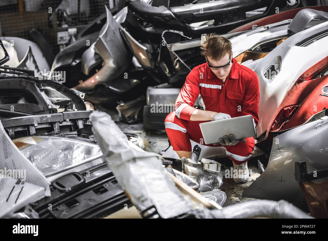 Vecchio impiegato di magazzino di parte di automobile che controlla l'inventario in garage. Il personale che lavora nella gestione delle parti auto del junkyard del motore di riciclaggio. Foto Stock