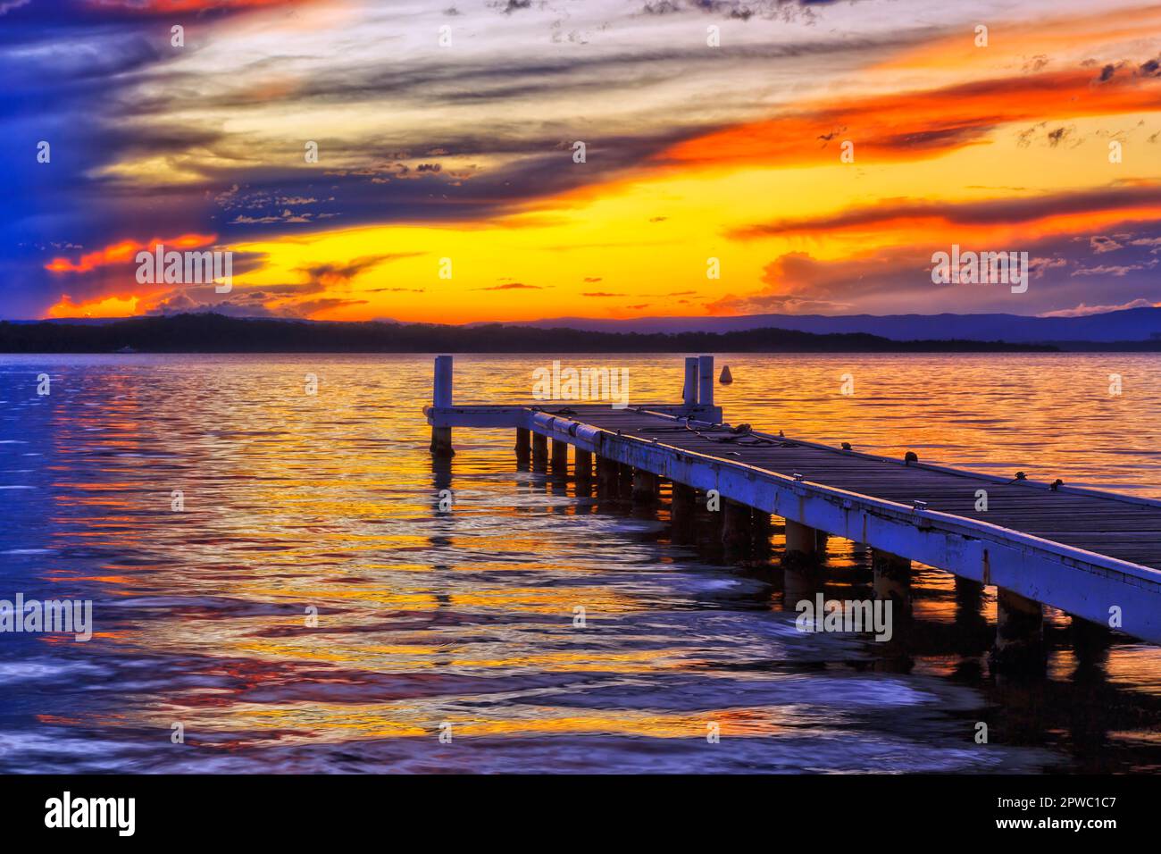 Luminoso tramonto coloufruil sulle acque del Lago Macquarie dal molo di legno della spiaggia di Murrays in Australia. Foto Stock