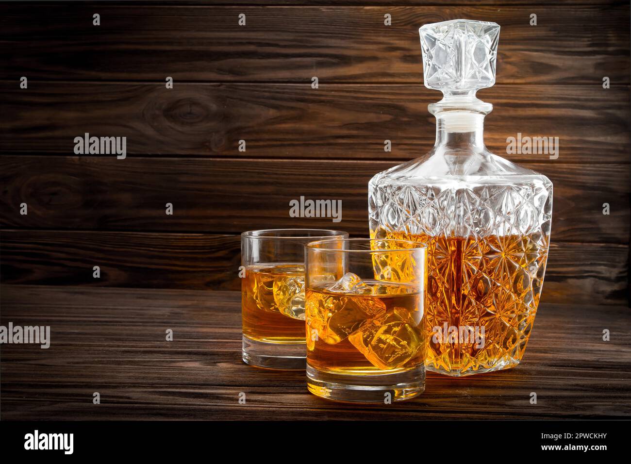 Bottiglia e due bicchieri con ghiaccio e whiskey su sfondo di legno Foto Stock