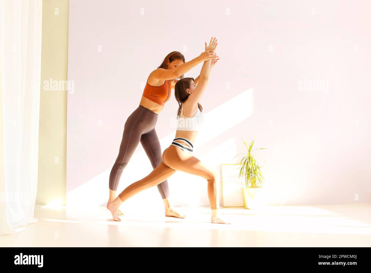 Donna adulta che aiuta la giovane femmina nello sport con fare yoga In Triangle posa e allungare le braccia Foto Stock