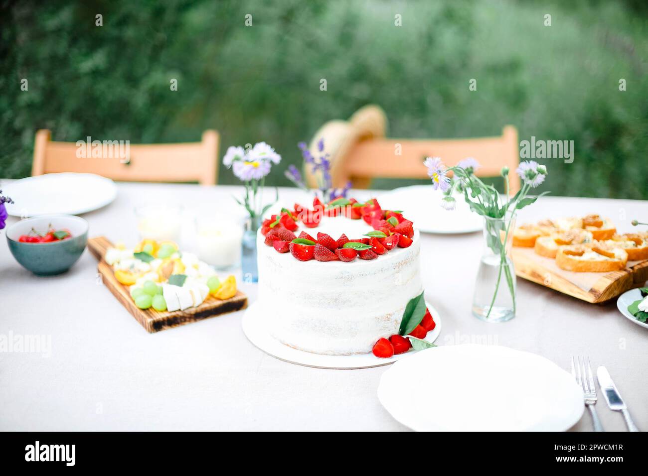Gustosa torta con frutti di bosco posta sul tavolo da banchetto vicino a fiori e stoviglie il giorno d'estate in giardino Foto Stock
