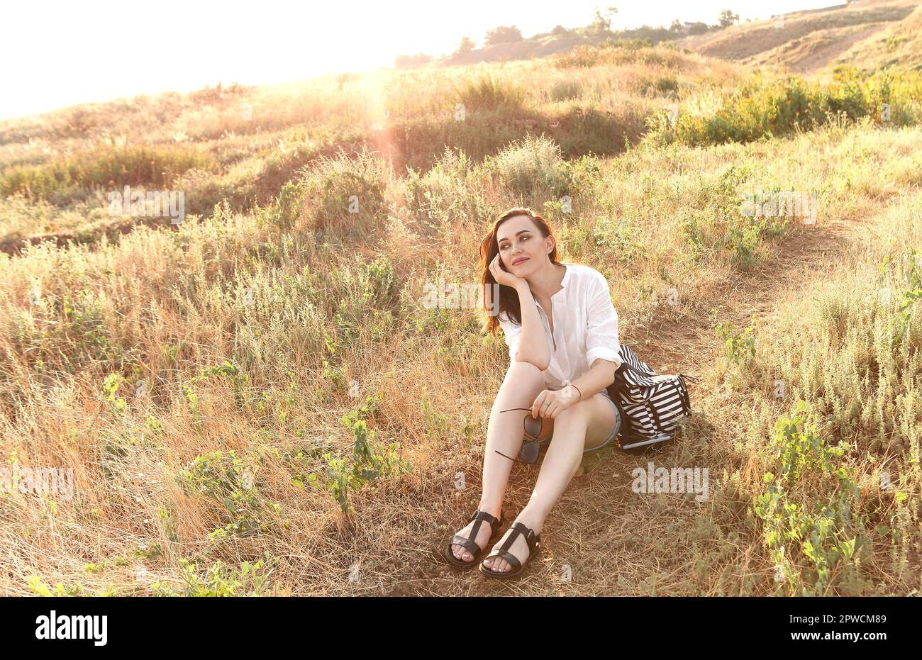 Giovane donna brunette viaggiatore seduta su erba su collina e. ammirate il paesaggio incredibile durante il tramonto in estate Foto Stock