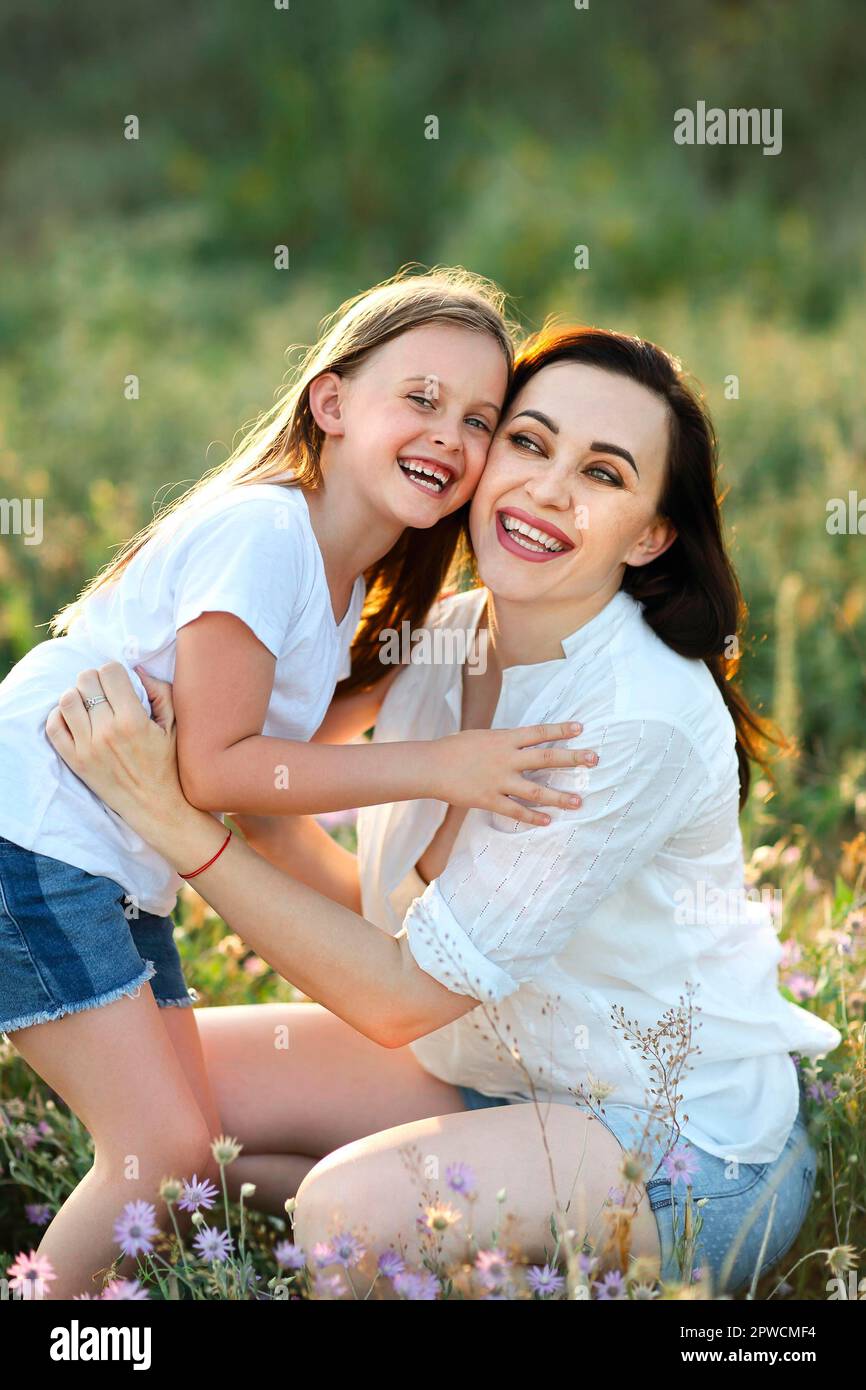 Sorridi madre e figlia coccolandosi dolcemente nel prato fiorente mentre trascorrete un fine settimana insieme in campagna e guardate la macchina fotografica Foto Stock