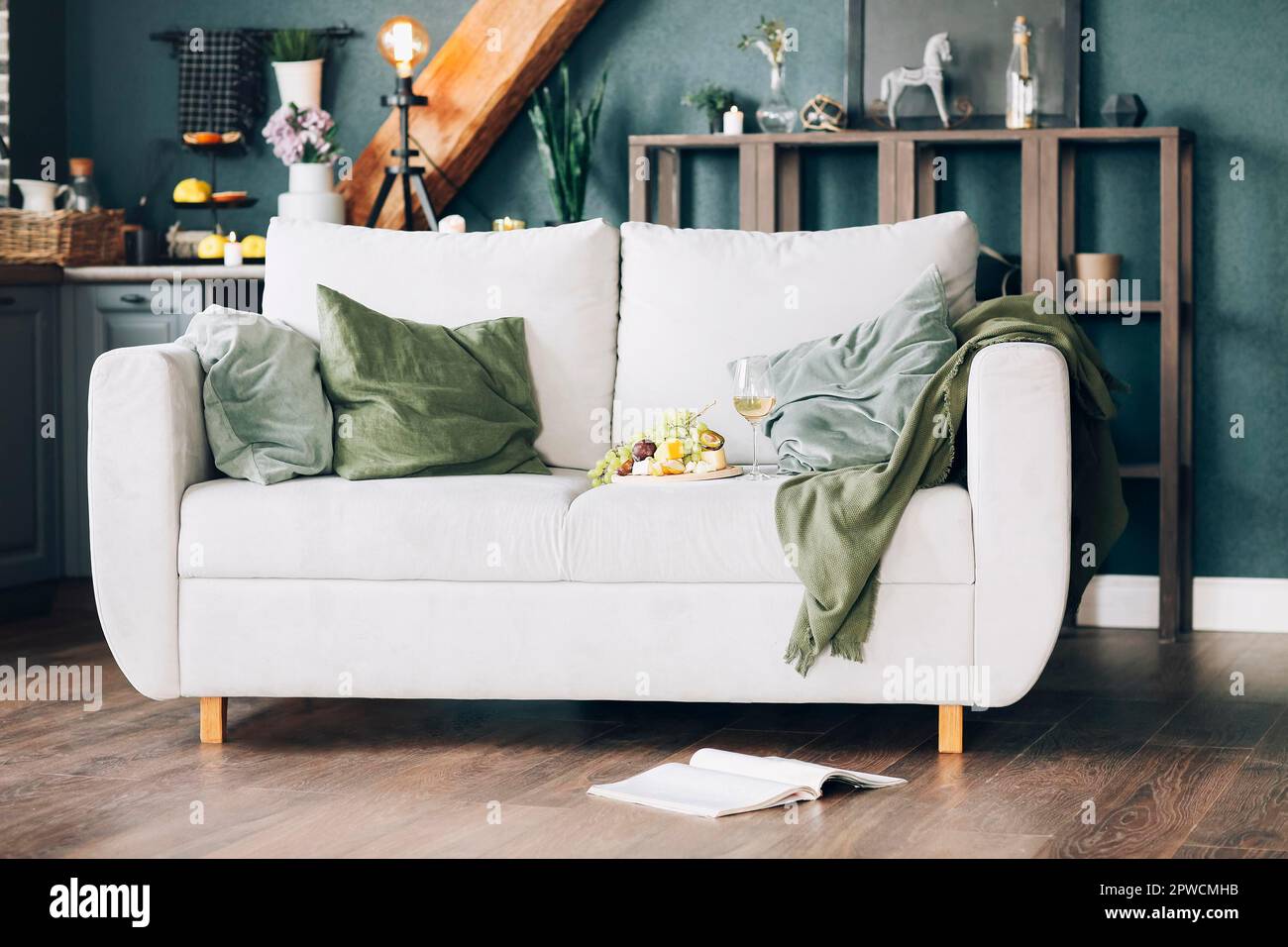 Piatto con frutta fresca e bicchiere di vino collocato vicino ai cuscini su un comodo divano nell'elegante camera di casa Foto Stock