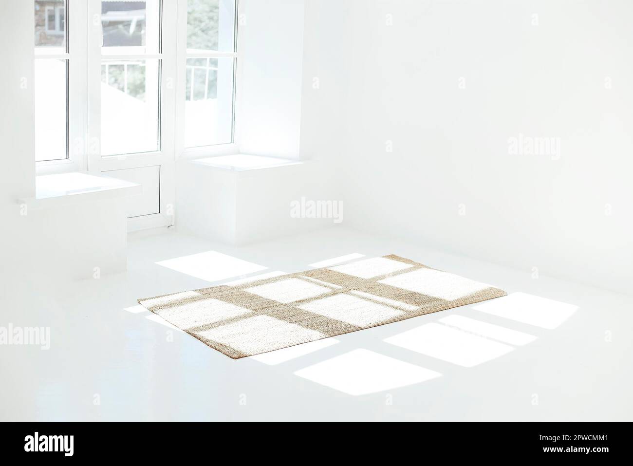 Moquette posta sul pavimento bianco vicino alla porta del balcone e finestre in camera vuota chiara Foto Stock