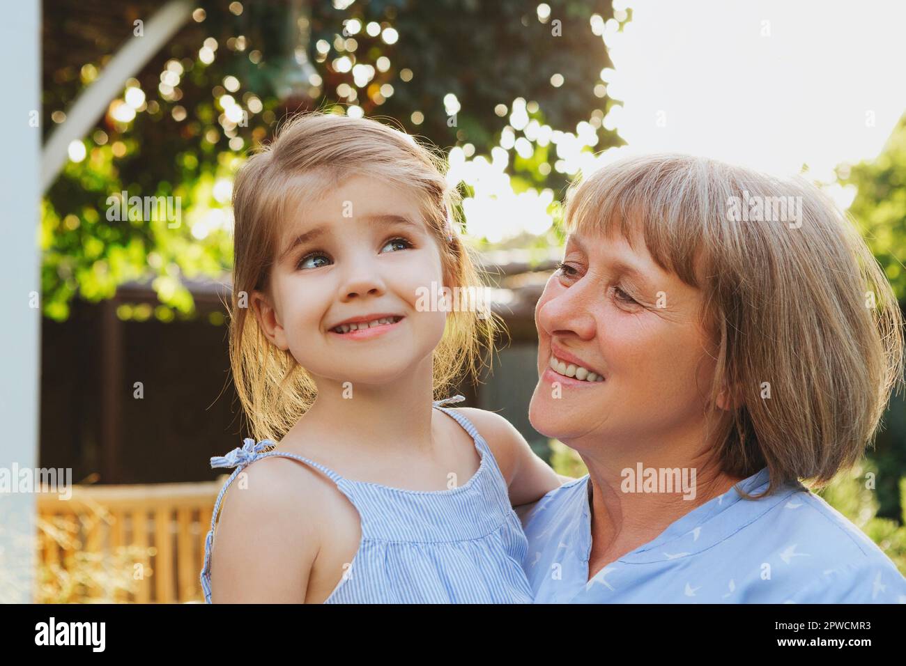 Felice di amare la nonna di mezza età che tiene la nonna del prescolare poco cute mentre si trova in piedi in giardino il giorno di estate, nonna con la ragazza piccola Foto Stock