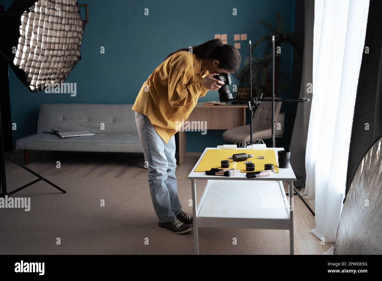 Fotografo con una fotocamera reflex per scattare una foto di un prodotto. Ripresa di prodotti di bellezza sul tavolo in casa studio Foto Stock