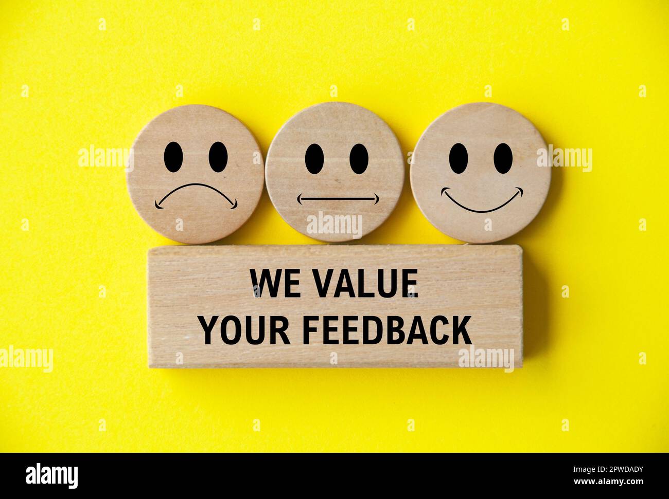 Apprezziamo il tuo testo di feedback su blocco di legno con facce emoticon felici, tristi e neutrali su cerchio di legno. Feedback dei clienti, soddisfazione ed valutazione Foto Stock
