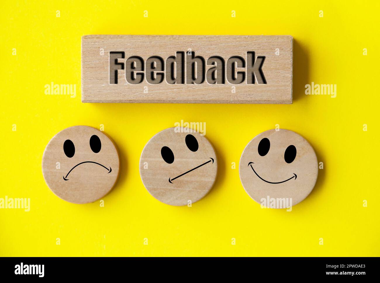Testo di feedback su blocco di legno con facce emoticon felici, tristi e neutrali su cerchio di legno con copertina di sfondo bianco. Feedback dei clienti, soddisfazione Foto Stock