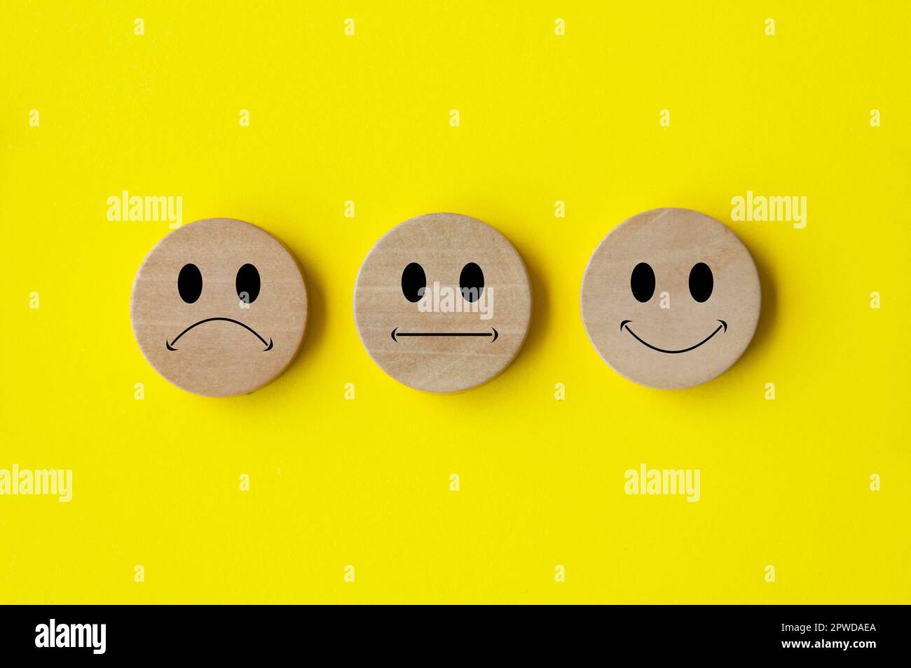 Faccine emoticon felici, tristi e neutrali su cerchio di legno con copertura di fondo gialla. Feedback dei clienti, soddisfazione, valutazione e concetto. Foto Stock