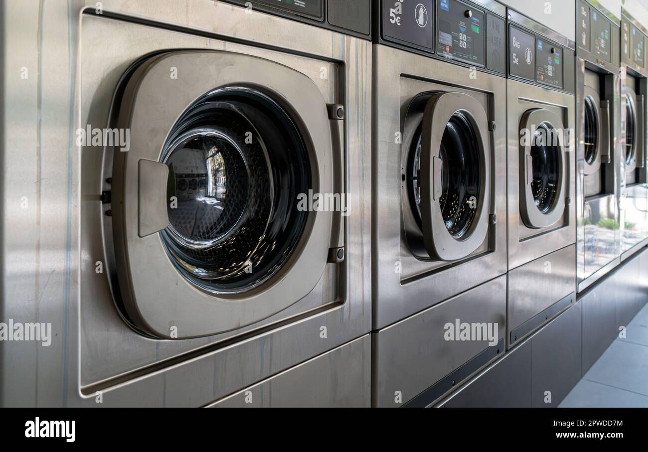 Lavatrici in una città urbana lavanderia per il lavaggio e l'asciugatura di vestiti, lenzuola e tovaglie in fila con le porte chiuse Foto Stock