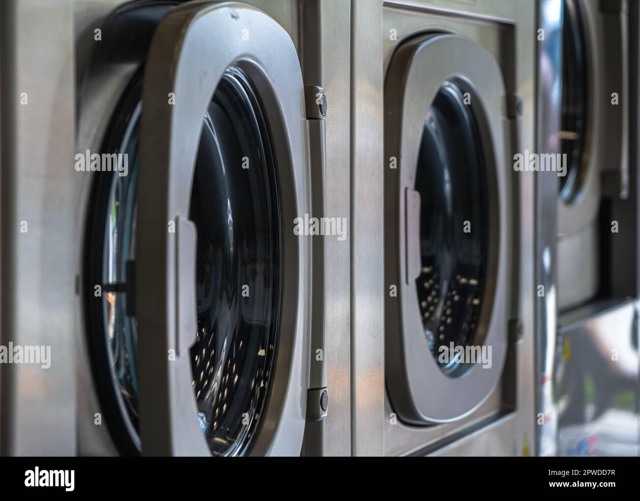 Lavatrici in una lavanderia urbana per il lavaggio e l'asciugatura di vestiti, lenzuola e tovaglie in fila con porta semi-chiusa Foto Stock