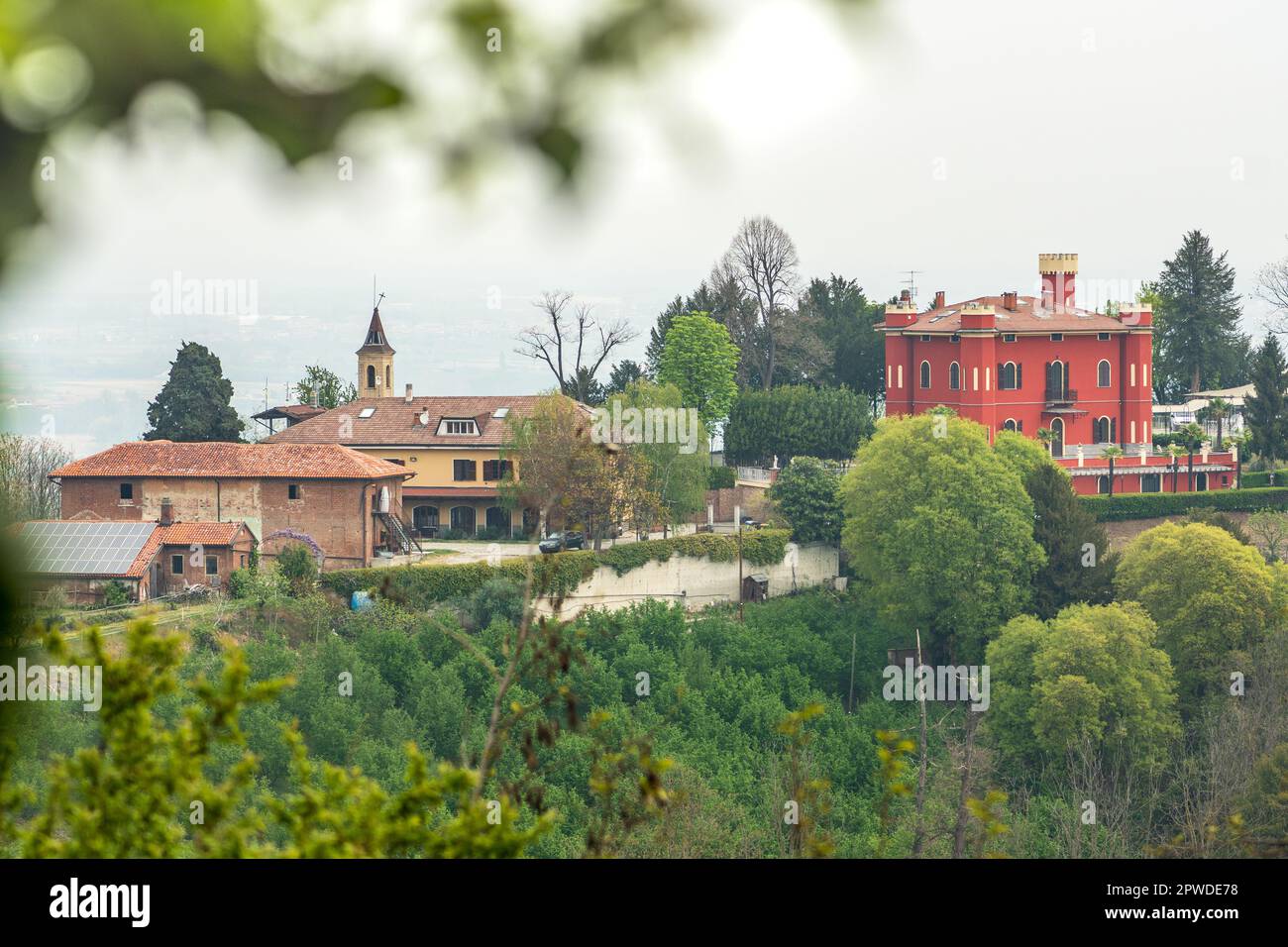 Vista panoramica sulle colline con vegetazione verde e un castello rosso o edificio dal Castello di San Sebastiano da po, Torino, Piemonte, Italia Foto Stock