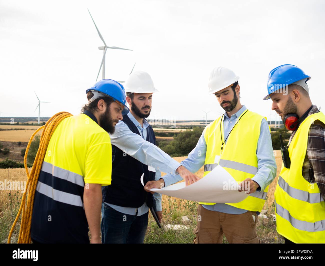 Gruppo di ingegneri maschi e lavoratori che guardano i progetti in un campo di mulini a vento Foto Stock