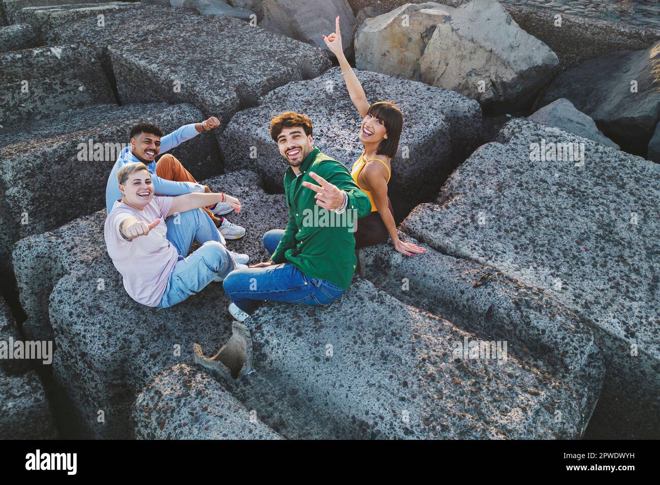 Un gruppo di quattro amici diversi festeggia insieme, facendo gesti di mani gioiose mentre si guarda la fotocamera. Ripresa aerea del drone. Foto Stock