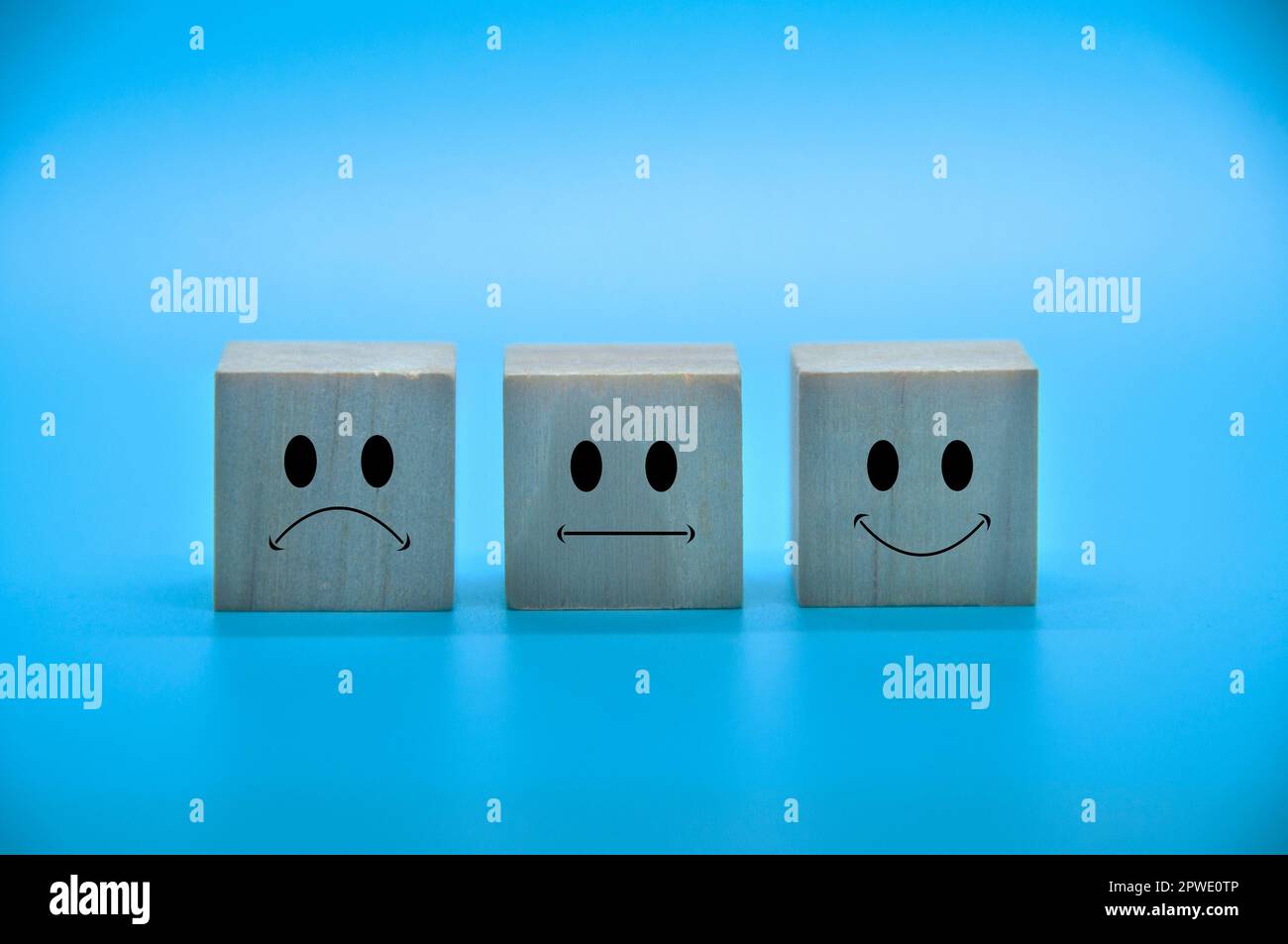 Faccine di emoticon tristi, neutrali e felici su cubi di legno con copertura di fondo blu. Soddisfazione del cliente e concetto di valutazione Foto Stock