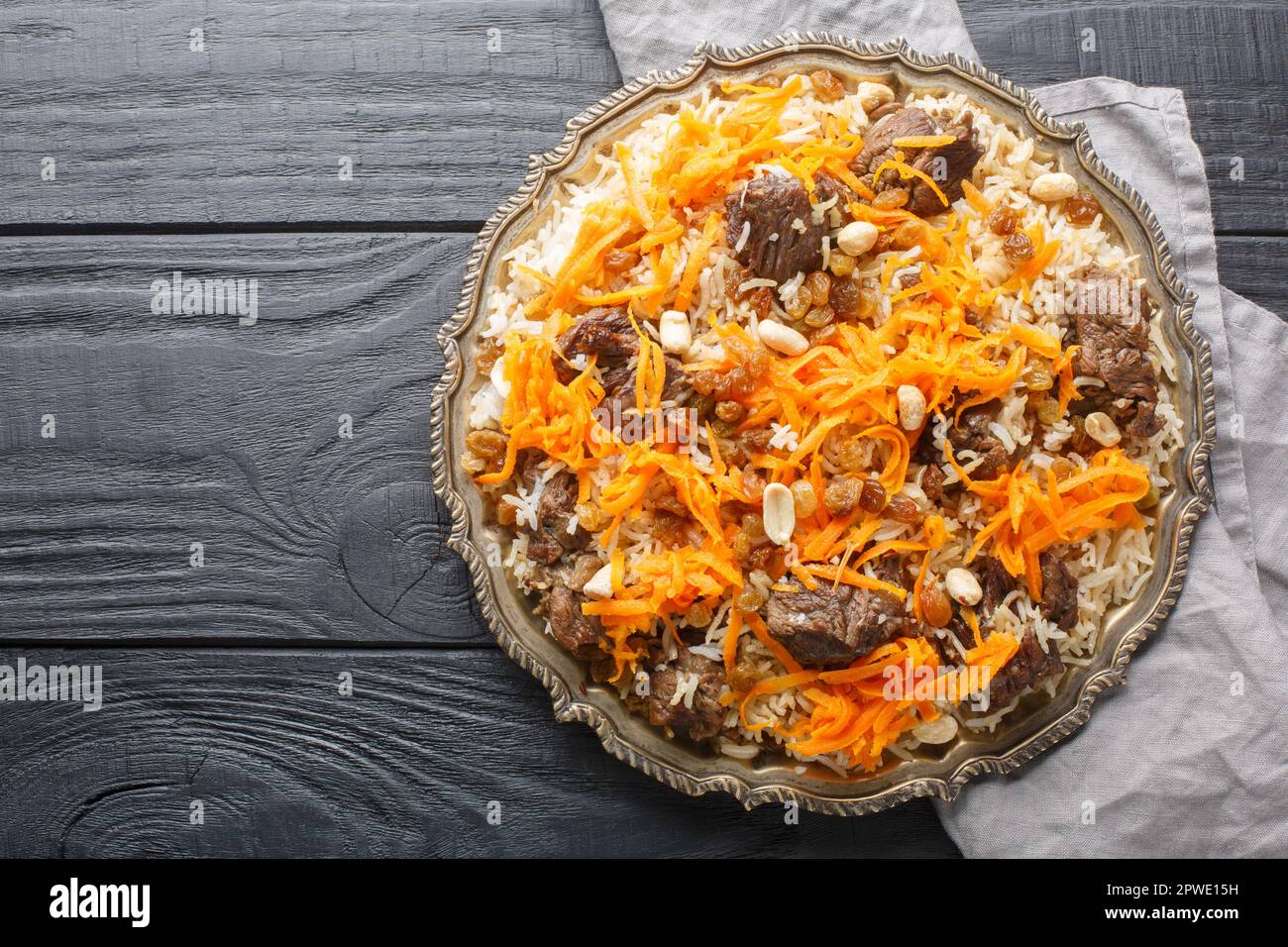 Tradizionale pilaf orientale con agnello sormontato da carote caramellate, uva passa e noci primo piano su un piatto su un tavolo di legno. vista dall'alto orizzontale fr Foto Stock