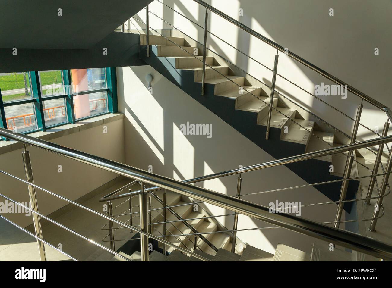 Scale in un edificio in cemento da ufficio in tonalità neutre, ricoperte di piastrelle in ceramica, con ringhiere in metallo lucido in acciaio inossidabile, ampia vetrata Foto Stock