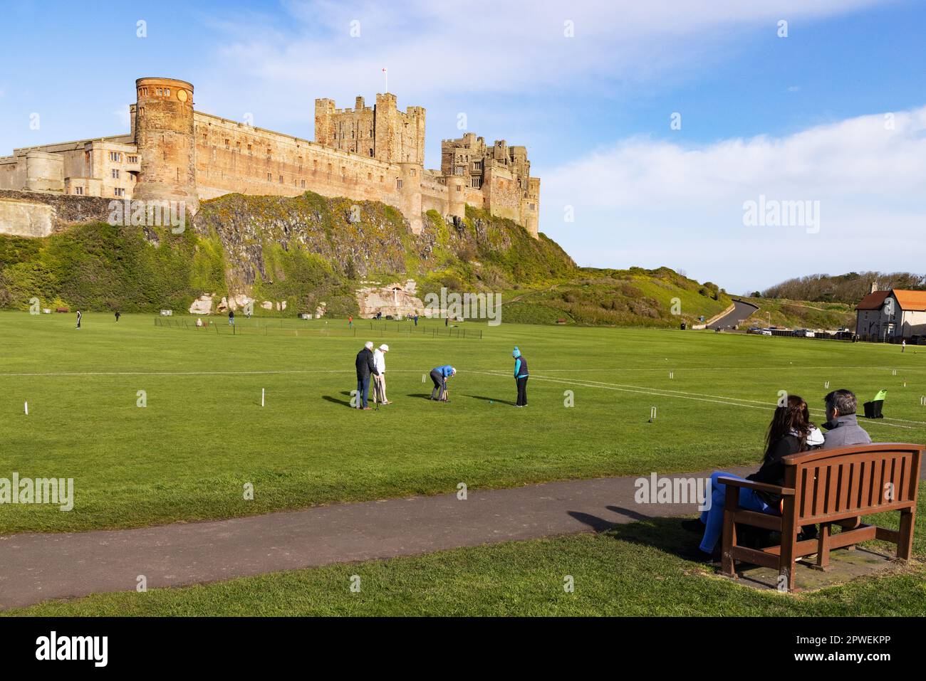 Castello di Bamburgh Northumberland Regno Unito; persone che giocano croquet di fronte al castello medievale del 11th ° secolo; villaggio di Bamburgh, Northumberland paesaggio, Regno Unito Foto Stock