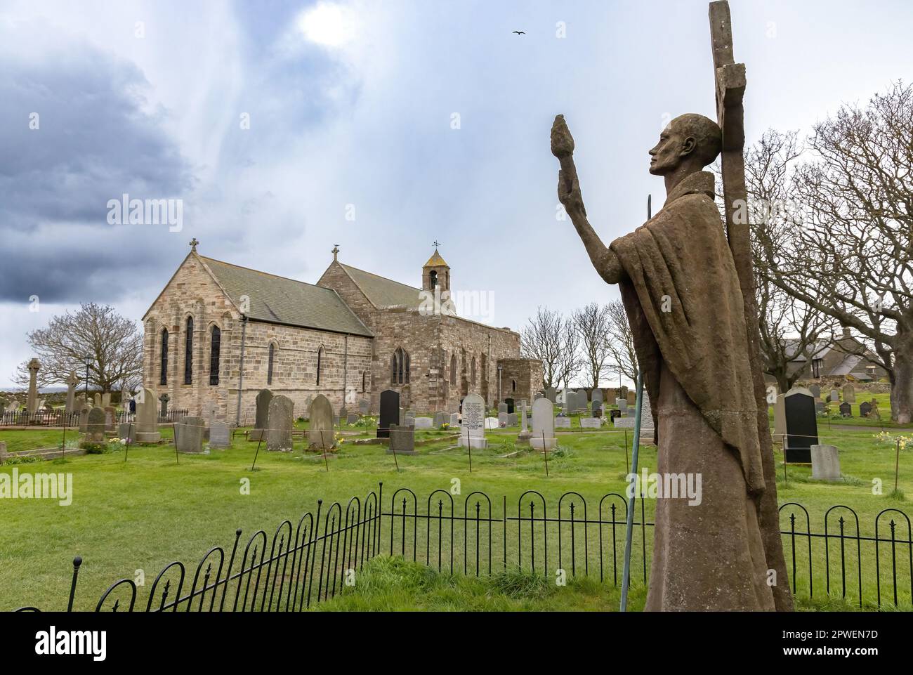 Chiesa di San Marys, o Chiesa di Santa Maria la Vergine, con la statua moderna di San Aidan nel cimitero, Lindisfarne o Holy Island, Northumberland UK Foto Stock