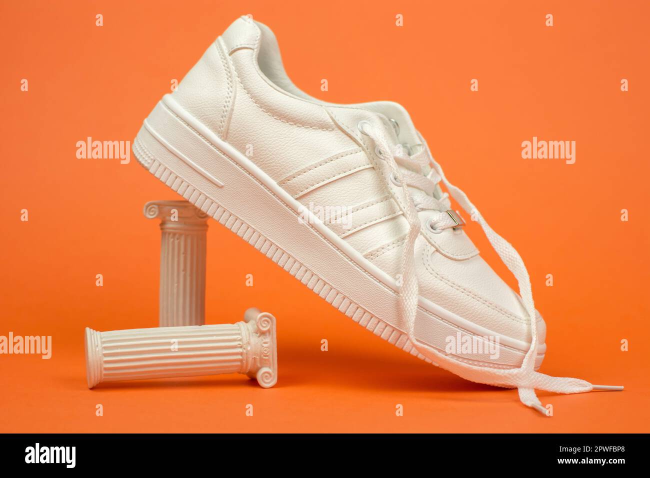 Elegante sneaker bianca con lacci senza allacciature. Sneaker bianca su sfondo arancione Foto Stock