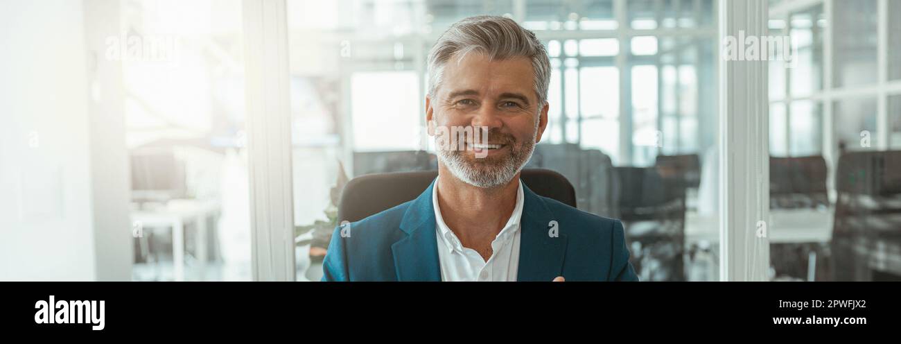 Uomo d'affari maturo sorridente che mostra le dita sollevate mentre si siede in ufficio Foto Stock