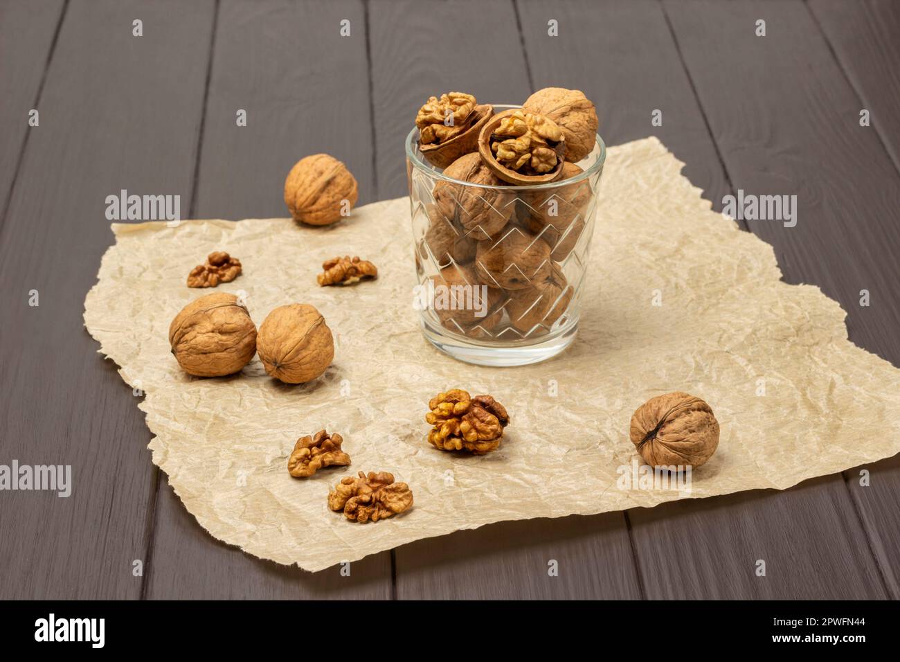 Noci intere e rotte in un vetro su carta. Gusci di noce e nocciolo sul tavolo. Sfondo di legno scuro. Foto Stock