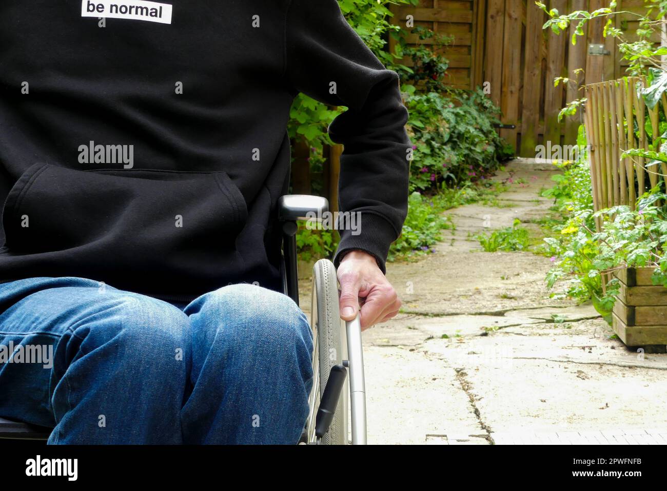 Una persona disabile su sedia a rotelle. Un uomo a mobilità ridotta in un vicolo con vegetazione. Foto Stock