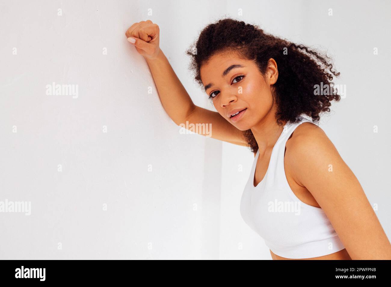 Primo piano studio ritratto di felice bella ragazza atletica di etnia africana in bianco top e leggings. Donna in forma sorridente in abbigliamento sportivo su bac bianco Foto Stock