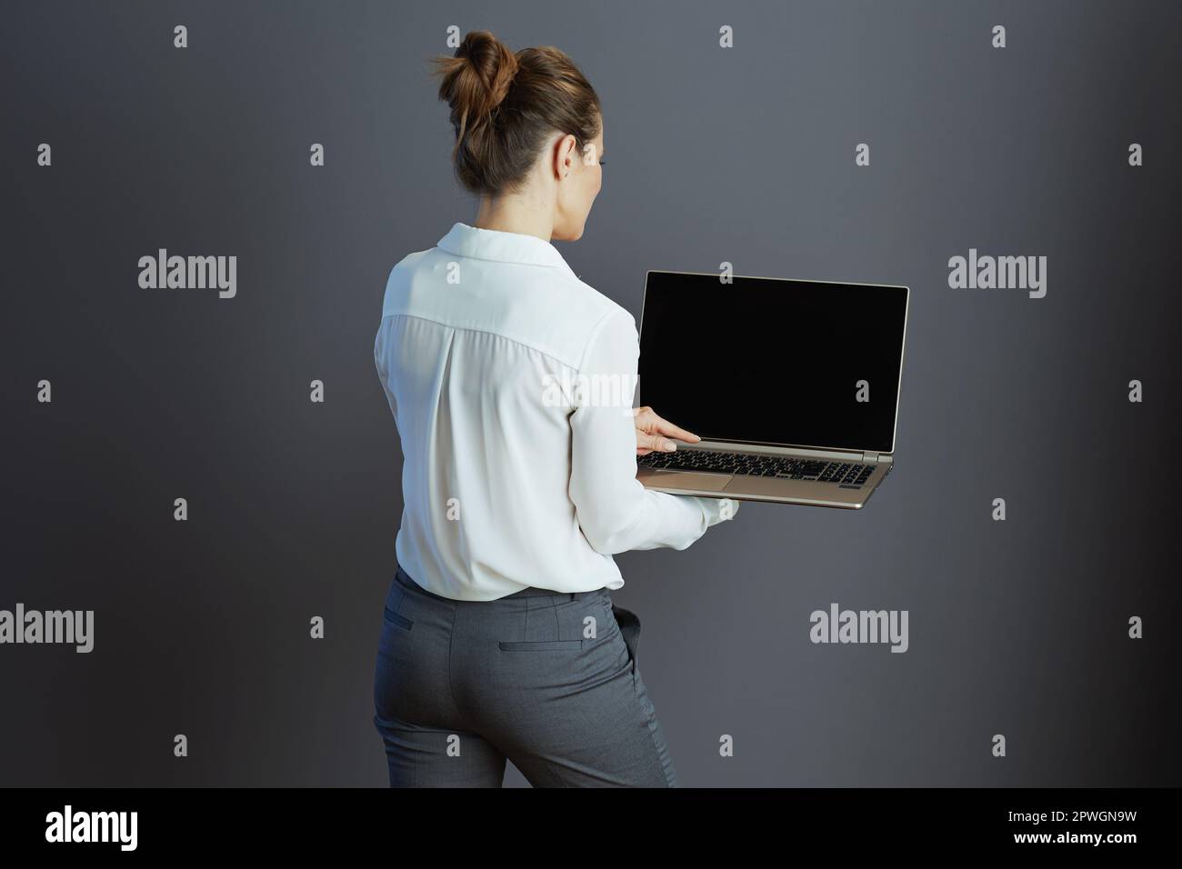 Vista da dietro una piccola donna di mezza età in blusa bianca con notebook su sfondo grigio. Foto Stock