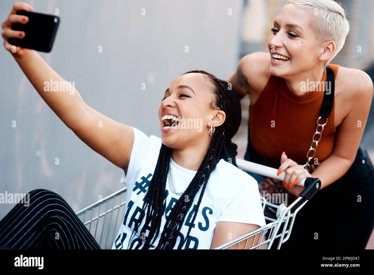 Le amicizie sono significate essere questo felice. due giovani amiche allegre che prendono un selfie mentre giocano con un carrello all'aperto Foto Stock