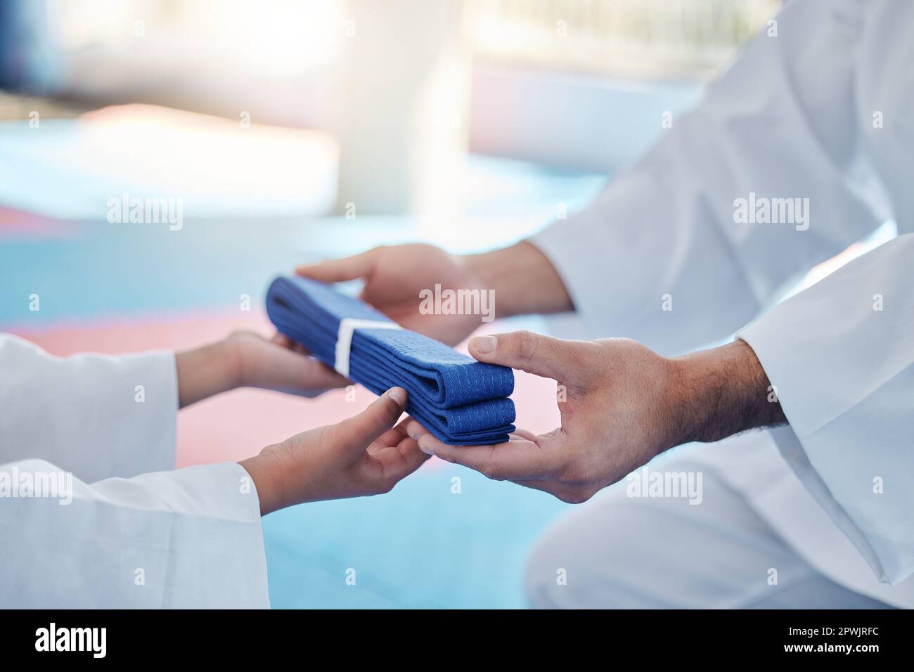 Un campione di karate in preparazione. un uomo irriconoscibile che ha consegnato al suo giovane studente una cintura di karate blu in uno studio Foto Stock