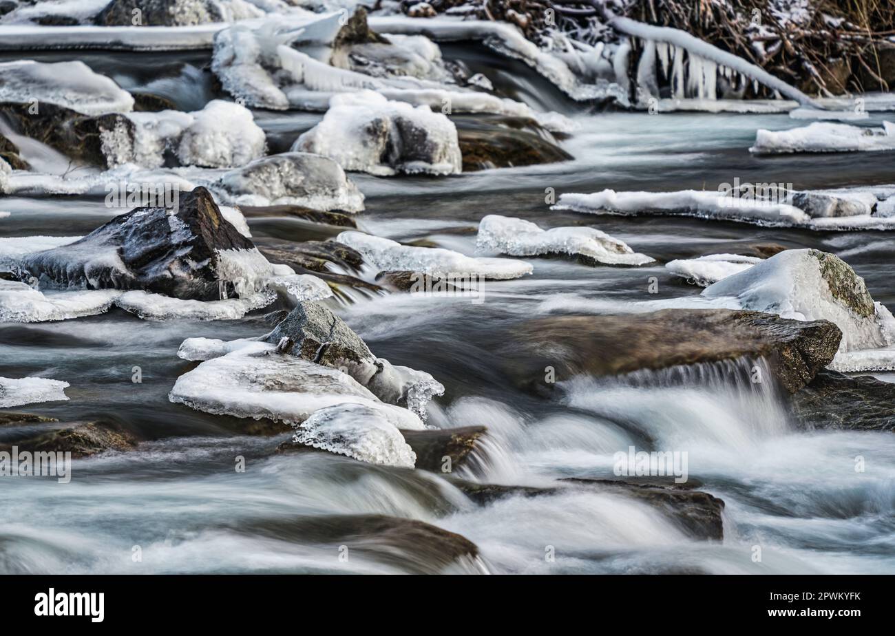 Fiume d'inverno che scorre su pietre coperte di neve e ghiaccio, dettaglio primo piano, foto a lunga esposizione. Foto Stock
